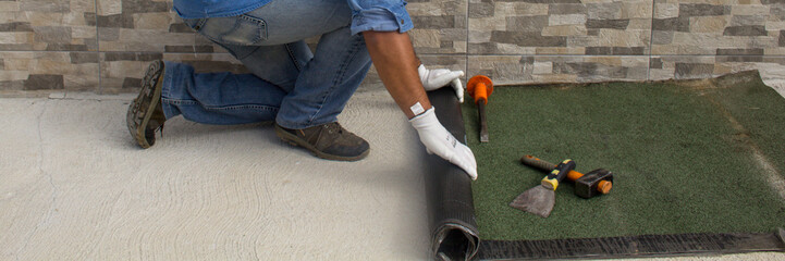 Construction worker at work while unrolling the tarred bituminous sheath to protect roofs and floors from bad weather and rain. Insulation in the construction sector. Horizontal banner 
