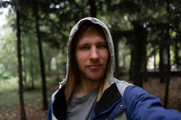 male bearded person traveling and hiking, taking selfie in the forest