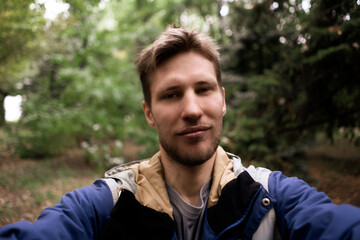 male bearded person traveling and hiking, taking selfie in the forest