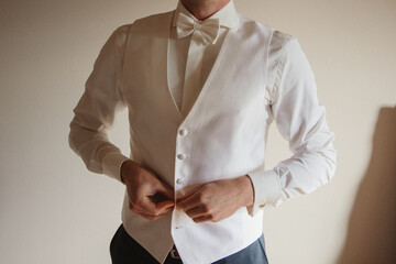A groom in a white vest and bow tie adjusting his attire, preparing for the wedding.
