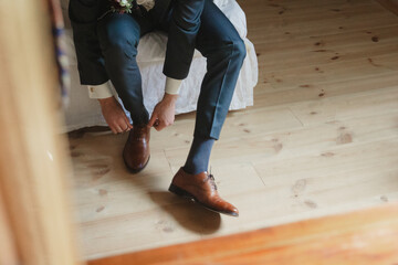 groom putting on brown leather shoes while wedding getting ready