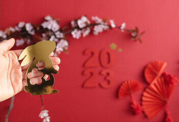 Chinese New Year, year of the rabbit. Red background with golden rabbit on paper cut on a mujecon hand plum branch decoration with flowers and fans.