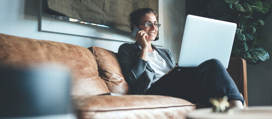Woman using laptop and talking on the phone, cozy studio apartment