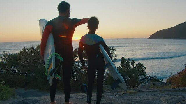 Family surfing. Father and son surfers stand on the coast and watch surfing spot on sunrise