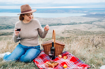Young woman with glass of wine having picnic in mountains on autumn day, back view