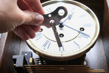 A hand holding a key to wind up a clockwork, vintage classic clock mechanism