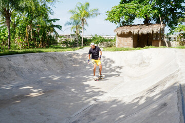 Fototapeta na wymiar Skater man riding on skateboard in bowl skatepark at sunny day. Tropical environment.