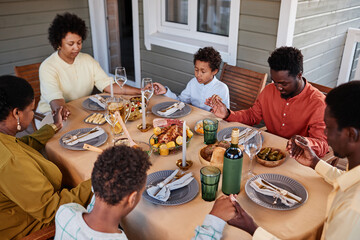 Portrait of African American family saying grace at dinner table and holding hands in cozy evening setting