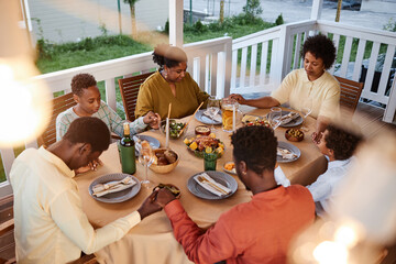 High angle view of African American family saying grace at dinner table outdoors and holding hands...