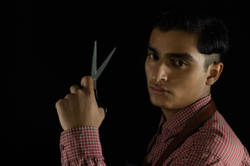 young latin barber with masculine expression on his face showing his scissors