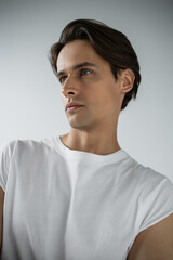 portrait of brunette man in white t-shirt looking away isolated on grey