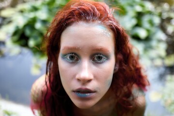 Close up portrait of beautiful sensual sexy young redhead woman mermaid in posing in river with water lilies. Fairytale story about water nymph.