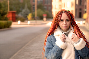 Portrait of positive young woman with dreadlocks on modern city street. Pretty female with bright hairstyle looking away, smiling.