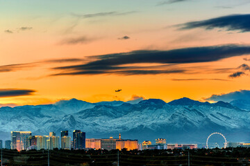 De skyline van Las Vegas in de winter met sneeuw bedekte berg en een straalvliegtuig dat opstijgt in de zonsonderganghemel