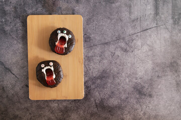 Scary halloween donut cake in chocolate glaze with teeth and eyes on concrete background for kids