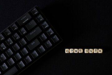Game over inscription on a black background next to a black gaming keyboard. Concept for eSports. Fatum, gambling addiction and the predetermination of the finale. - obrazy, fototapety, plakaty
