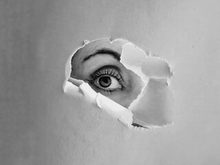 Grayscale shot of a female eye looking behing a torn paper