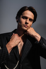brunette man looking at camera while adjusting trendy suit on dark grey