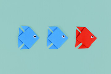Red origami paper fish swimming in front of blue fish. Concept for discovery and strong leadership