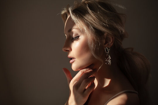 Portrait of a beautiful girl with an evening elegant hairstyle and cmokey eyes makeup, a woman dressed in a silk shirt and earrings. Female model posing in the morning rays of the sun