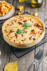 Homemade quiche or tart with chanterelles on rustic wooden background.