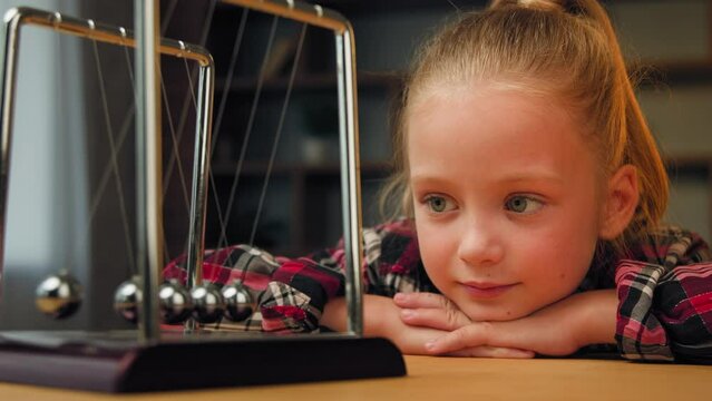 Cute little child toddler beautiful young restful school girl sit on psychotherapy session indoors pretty blonde kid daughter looking at magnetic swinging metal steel balls calm down therapy hypnosis