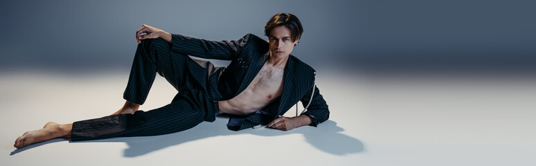 stylish man in suit with pearls and hairy chest posing on dark grey background, banner