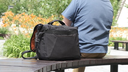 Bag is on park bench next to its owner. Man is resting with photo bag next to him.