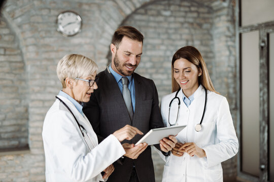 Two Doctors And Mid Adult Businessman Working On Digital Tablet In The Office. 