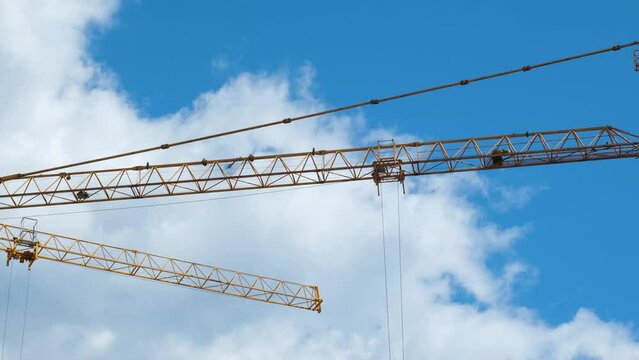 Construction crane working in front of cloudy open sky, 4k 60 fps construction site concept video, close-up two cranes carrying the load, 