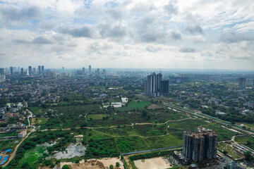 aerial drone shot over gurgaon showing monsoon clouds with light rays falling on ground crowded with homes houses, sohna highway feilds and water pools around under construction buildings