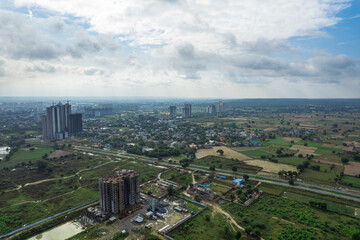 aerial drone shot over gurgaon showing monsoon clouds with light rays falling on ground crowded with homes houses, sohna highway feilds and water pools around under construction buildings