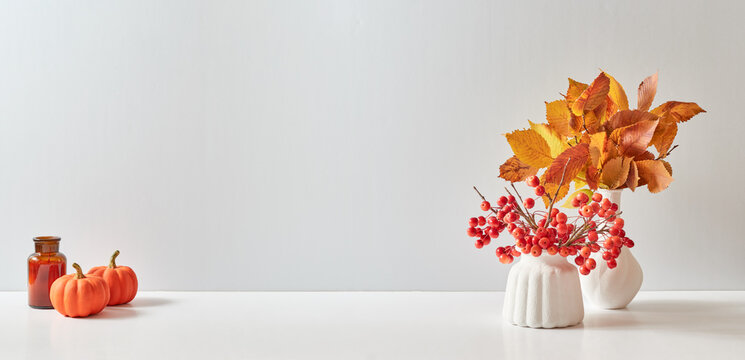 Home interior with decor elements. Colorful autumn leaves in a vase on a light background. Mock up for displaying works