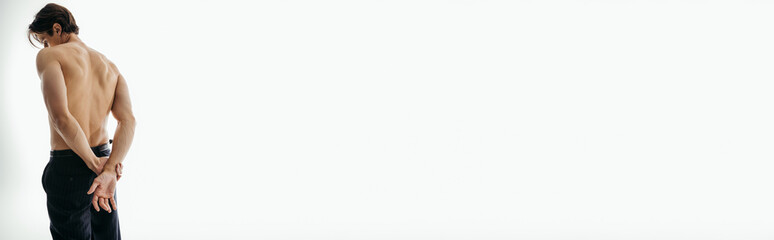 Obraz premium back view of muscular and shirtless man in black trousers posing on white background, banner