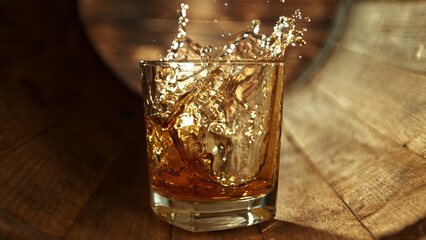 Ice cube falling into glass of whisky in wooden barrel.