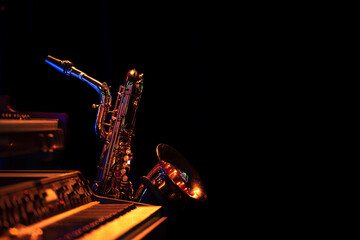 Saxophone in black environment standing behind a piano keyboard