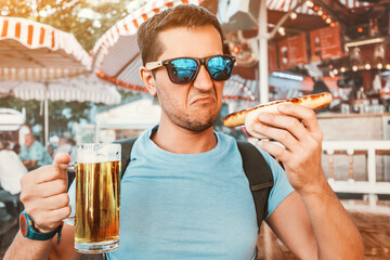man drinking beer and eating traditional german bratwurst - hotdog. Making funny Not Bad face...