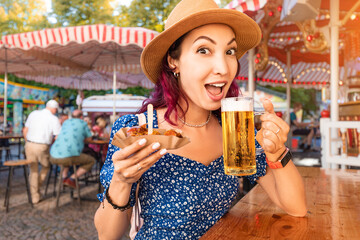 Happy girl drinking beer and eating traditional german currywurst meal at funfair and street food...