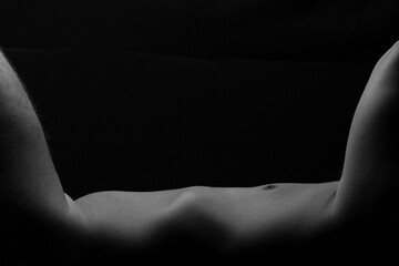 exposed torso and chest of laying nude male model balanced by raised arm and leg against black horizontal background