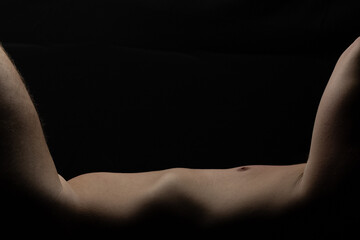 Attractive man posing naked in fragment of nude body lying against black background with negative or copy space above for advertising