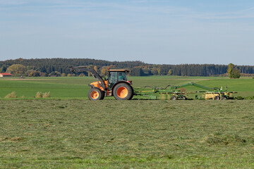 The tractor in the field loosens the cut grass with a rotary harvester for better drying.