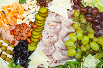 Background of food laid out on a tray. Ham, cheese, prunes, almonds, raisins, grapes, mandarin...