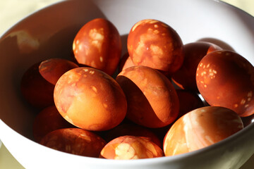 Easter eggs dyed with onion peels with a pattern of fresh plants on white background. White bowl. Spring time