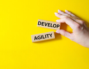 Develop agility symbol. Concept word Develop agility on wooden blocks. Beautiful yellow background. Businessman hand. Business and Develop agility concept. Copy space