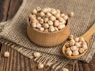 Wooden bowl and wooden spoon full of chickpeas on a wooden background.