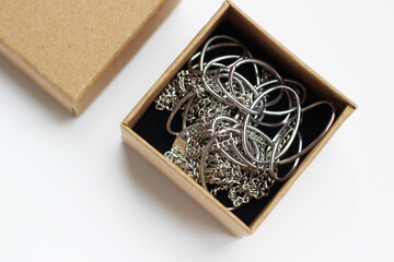 Opened craft box with metal bijouterie inside, horizontal photo on light background, top view. Beauty and fashion industry, round big and little rings