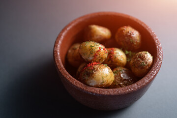 roasted potatoes with herbs and spice in clay bowl on black background