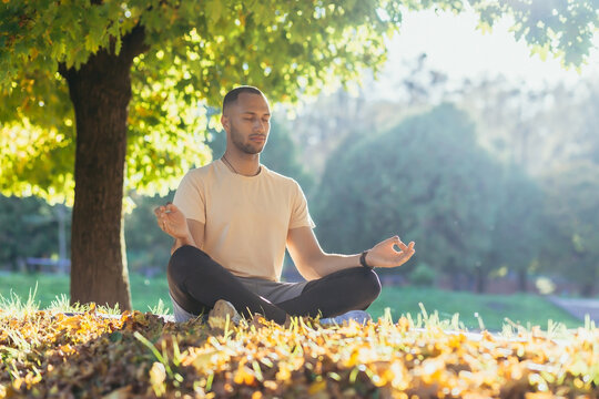 A young man meditates in the park at sunset, an athlete in the lotus position sits on a sports mat under the autumn trees. - Powered by Adobe