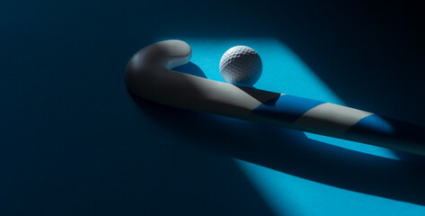 Field hockey stick and white ball with natural lighting on blue background. Sport team concept....