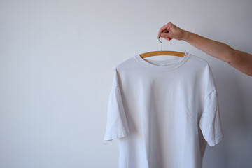 White t-shirt on a hanger in hands on a light background. Space for copy. Clothes on hangers
